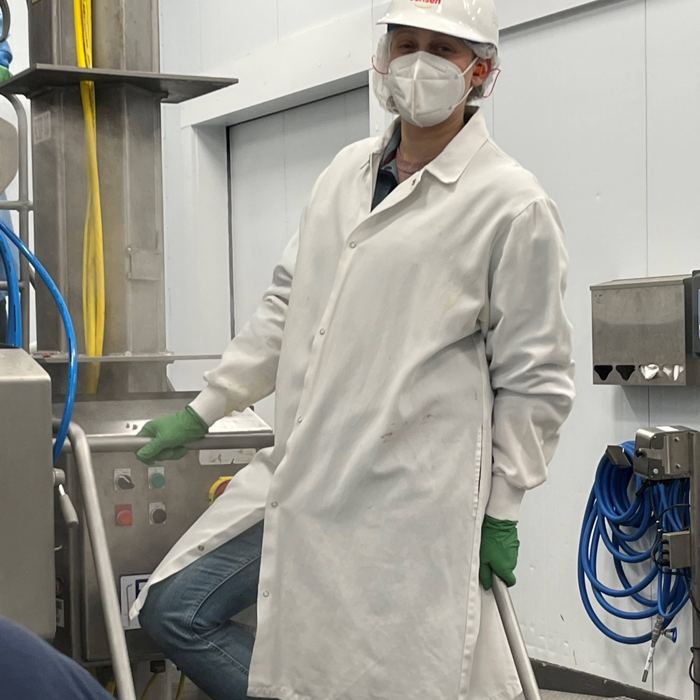 Julia on a production floor in a white coat, hairnet and mask