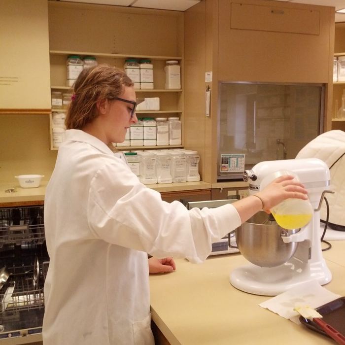 Julia in a lab coat pouring into a stand mixer