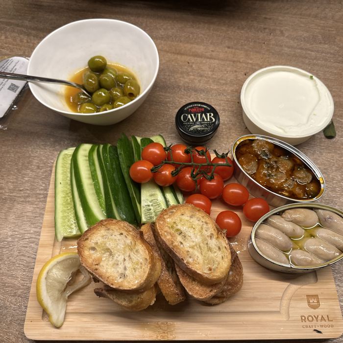 A wooden board of bread, cucumbers, tomatoes and olives