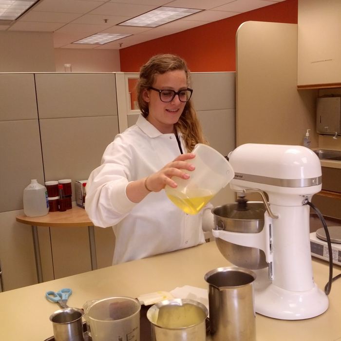 Julia in a lab coat pouring into a stand mixer