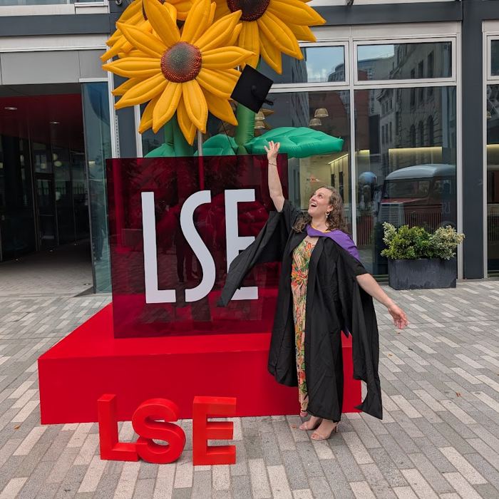 Julia throwing her graduation cap beside giant LSE letters and a sunflower