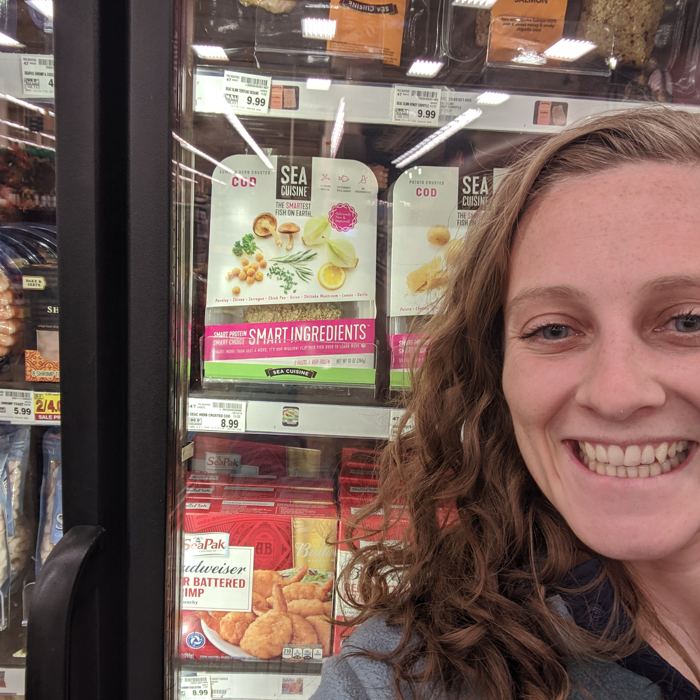 Julia grinning in front of a freezer case stocked with Sea Cuisine products she developed